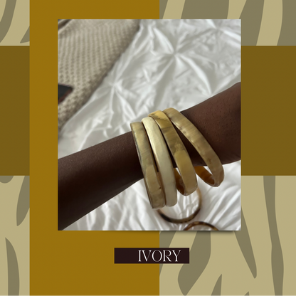A promotional graphic for 'Summa Bangles' showing a stack of four ivory-colored bangles on a person's wrist, set against a white textured fabric background. The graphic features a gold and beige patterned border with text reading 'SUMMA BANGLES ARE HERE' at the top and 'IVORY' at the bottom.