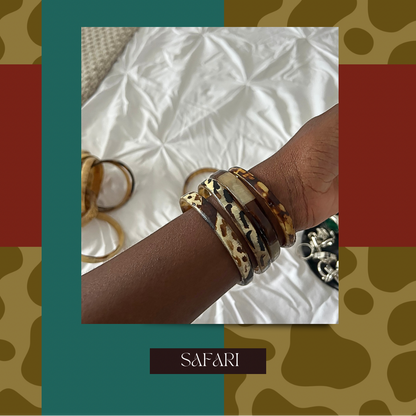Promotional graphic for 'Summa Bangles Are Here' featuring a close-up of a person's wrist wearing multiple bangles, including leopard print and tortoiseshell styles, set against a white fabric background. The graphic has a bold border with teal, rust red, and brown safari-patterned sections, with the text 'SUMMA BANGLES ARE HERE' at the top and 'SAFARI' at the bottom.